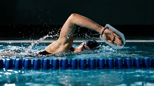 Competitive swimmer using hand paddles mid-freestyle stroke in a training pool
