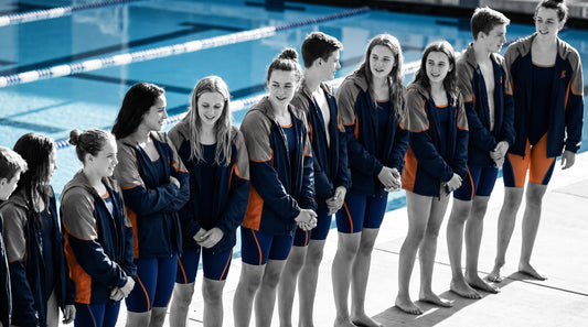 Youth swim team on an outdoor pool deck in matching custom team warm-up jackets and team swimsuits