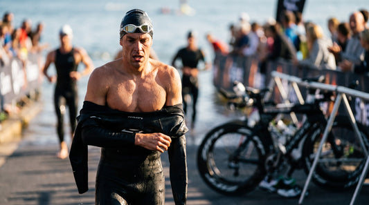 Triathlete peeling off a wetsuit while running into transition with goggles pushed up