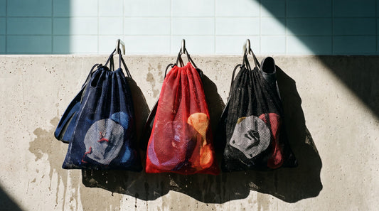 Mesh equipment bags hanging on a pool wall loaded with fins, paddles and pull buoys