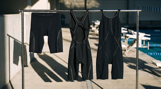 Racing tech suits on a poolside rack including a jammer and open-back and closed-back knee suits