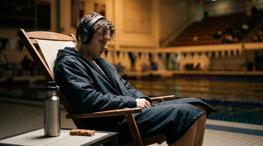 Swimmer resting between events at a meet in a swim parka with water and a snack