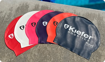 Set of Kiefer Aquatic swim caps in various colors on a concrete surface.