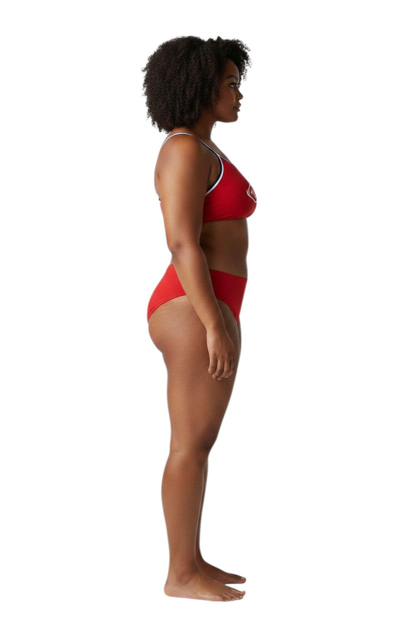 A model wearing Kiefer tri-color red bikini with white and blue trim, side view, studio background.