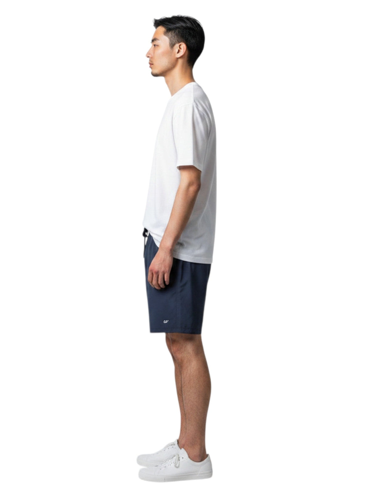 Male lifeguard wearing Kiefer white short sleeve crew neck rashguard and navy shorts, side view.